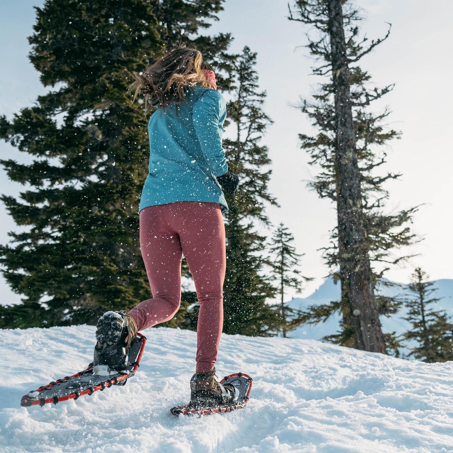 Woman hiking in snow wearing Women’s Elite 25 teal snowshoes