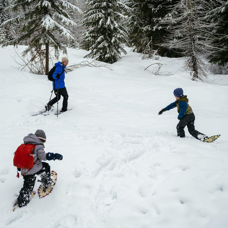 Child walking in snow wearing youth snowshoes on a winter trail